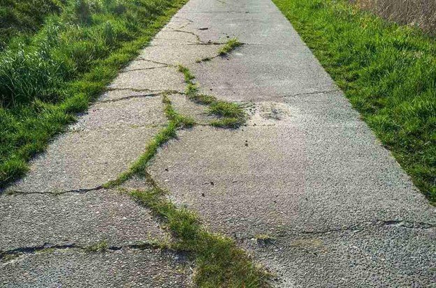 Cracked and damaged concrete driveway with visible wear and weeds growing through surface in Medina, OH